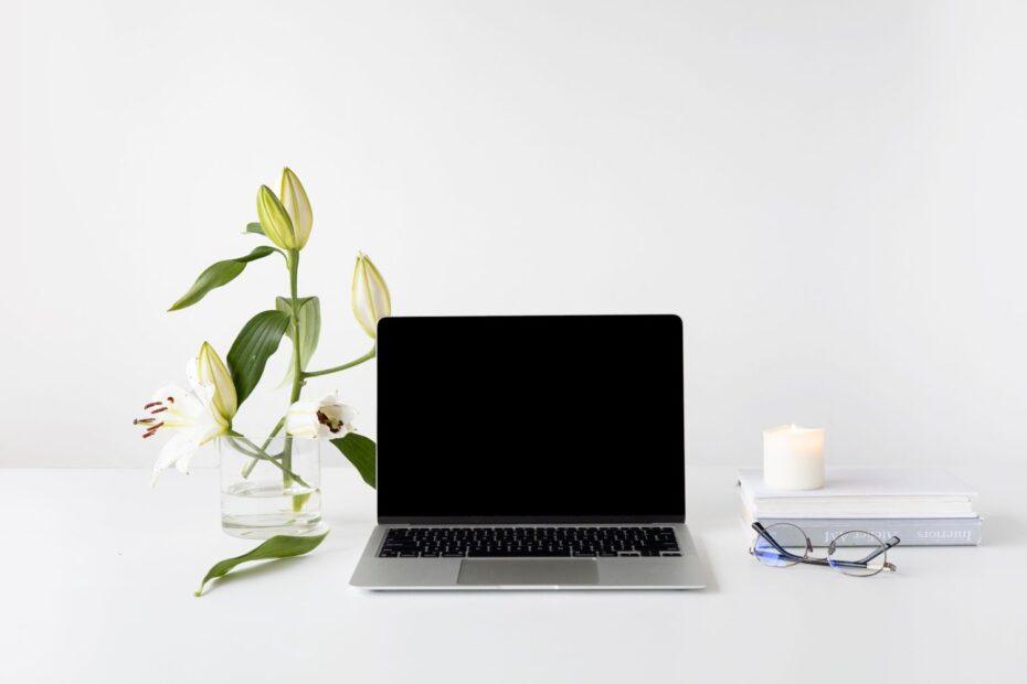 Elegant minimalist desk setup with laptop, white lilies, books, and candle.