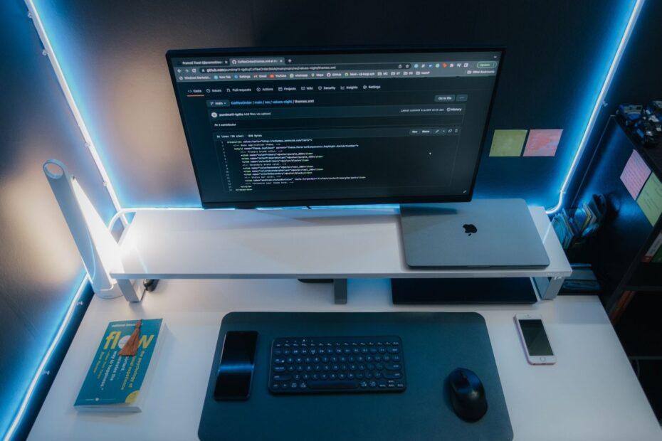 A minimalist workspace with a computer setup, gadgets, and neon lighting for a sleek modern look.