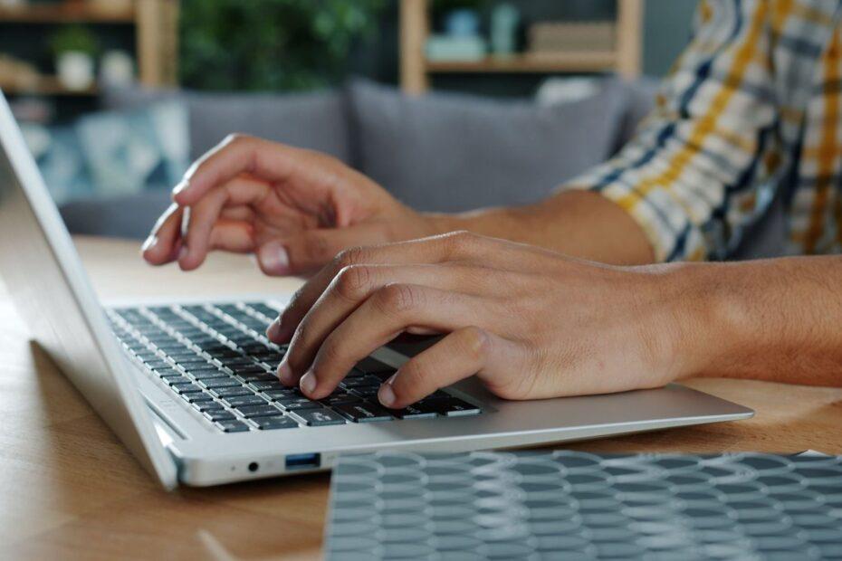 Close-up of hands typing on a laptop indoors, ideal for work-from-home themes.