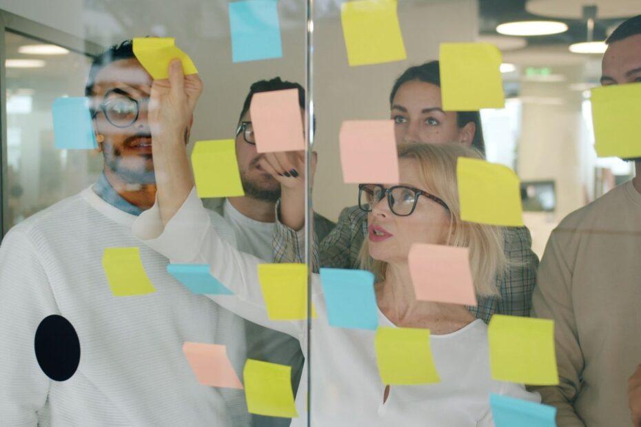 Diverse team brainstorming with colorful sticky notes on glass in modern office.